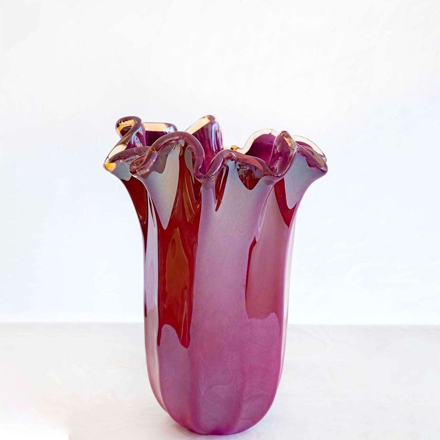 Eine große, glänzende, violette „Fazzoletto“-Vase (H 31, Ø 20 cm) von Murano Dream – handgefertigtes Murano-Glas mit gewellten Rändern –, präsentiert auf einer hellen Unterlage vor einem schlichten weißen Hintergrund.