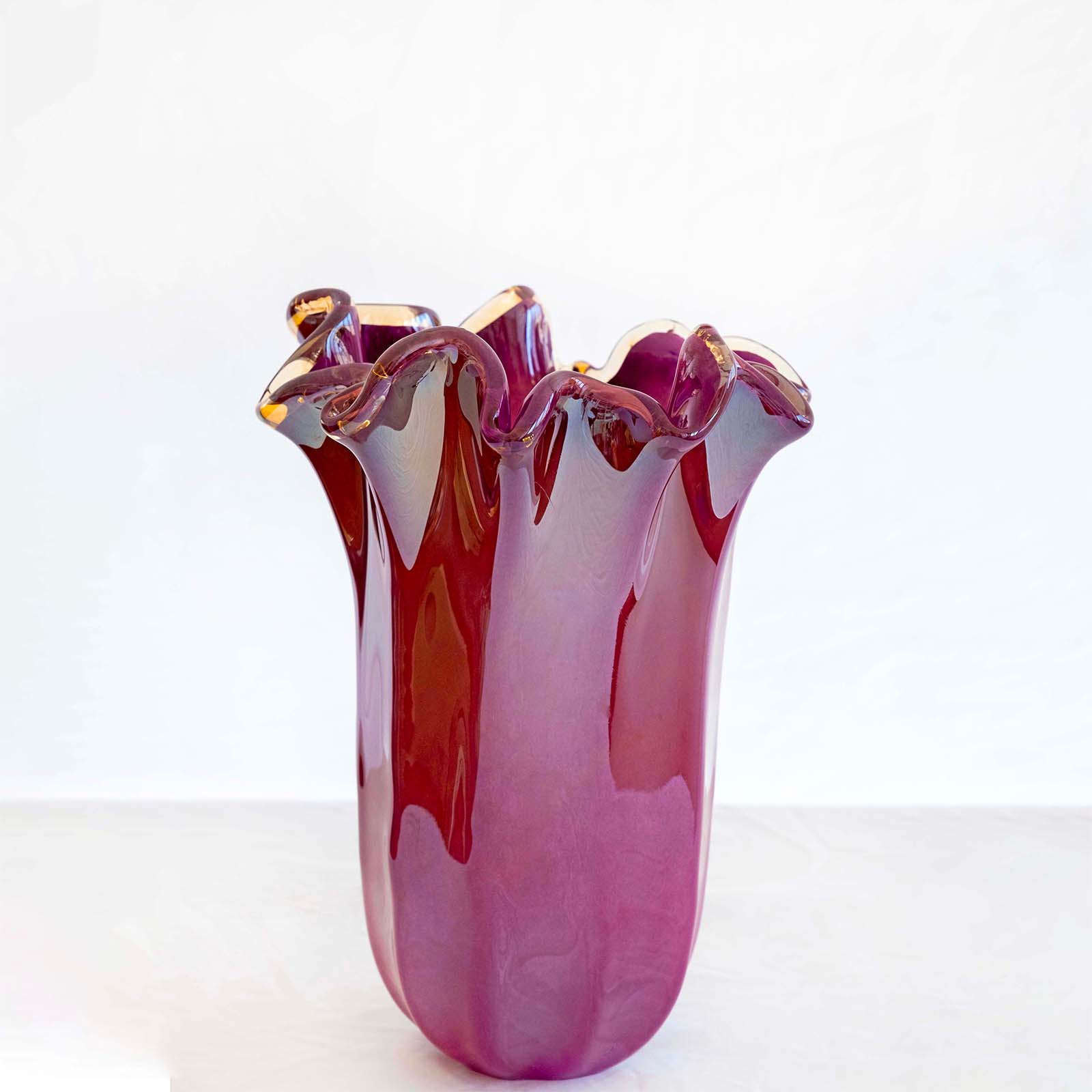 Eine große, glänzende, violette „Fazzoletto“-Vase (H 31, Ø 20 cm) von Murano Dream – handgefertigtes Murano-Glas mit gewellten Rändern –, präsentiert auf einer hellen Unterlage vor einem schlichten weißen Hintergrund.