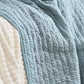 Eine Nahaufnahme eines Bettes mit der IB Laursen Quilt Decke hellblau mit Kreuzstich, drapiert über eine cremefarbene Steppdecke und Kissen, ideal für skandinavische Wohndeko.