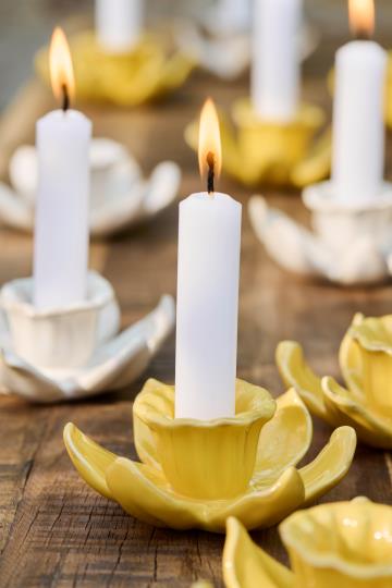 Weiße Kerzen leuchten in gelben und weißen blumenförmigen Keramikhaltern, die mit dem Ib Laursen Kerzenhalter aus Keramik Narzisse 'Buttercreme', von IB Laursen, auf Holz arrangiert, für einen frischen Frühlingsdeko Steinzeug Look sorgen.