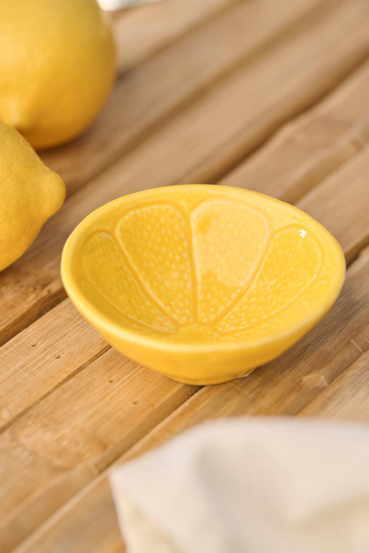 Die Ib Laursen | Schale mini Zitrone aus Steingut von IB Laursen steht auf einer hölzernen Unterlage, deren gelbes Zitronenscheibendesign mit frischen Zitronen und einem leichten Tuch harmoniert.
