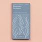 Eine blaue Piccolo Seeds | Rosmarin Common Packung mit botanischen Mustern, beschriftet mit 150 Samen (Rosmarinus officinalis), ein mediterranes Kraut und immergrüner Strauch von Piccolo Seeds, auf einem pfirsichfarbenen Hintergrund.
