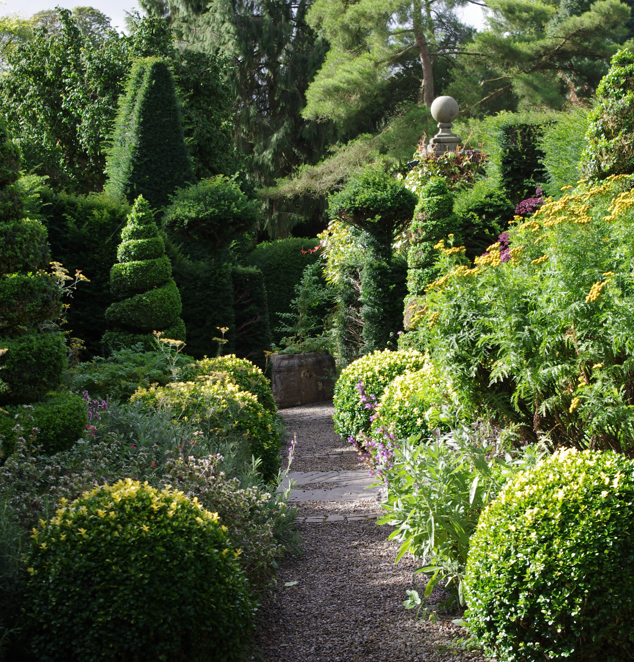 Ein schmaler Schotterweg schlängelt sich durch die Di. 16.2.2027 | 14.30 – 15.30 Uhr AFTERNOON TEA Yorkshires vielfältige Gartenpracht mit kunstvoll geschnittenen Formsträuchern und blühenden Pflanzen, die sich perfekt für den Nachmittagstee eignen.