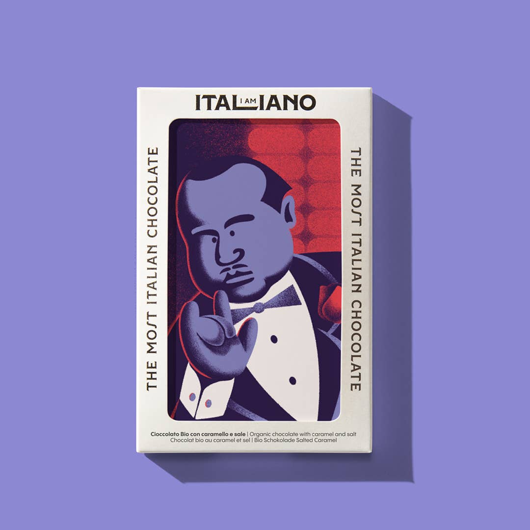 Eine Schachtel I AM ITALIANO | 'Padrino' Bio-Schokolade mit Karamell und Salz, mit einem Mann im Smoking, der eine Handbewegung macht und THE MOST ITALIAN CHOCOLATE auf den Seiten. Genießen Sie diesen Bio-Riegel in einer auffälligen lila-roten I AM ITALIANO-Verpackung.