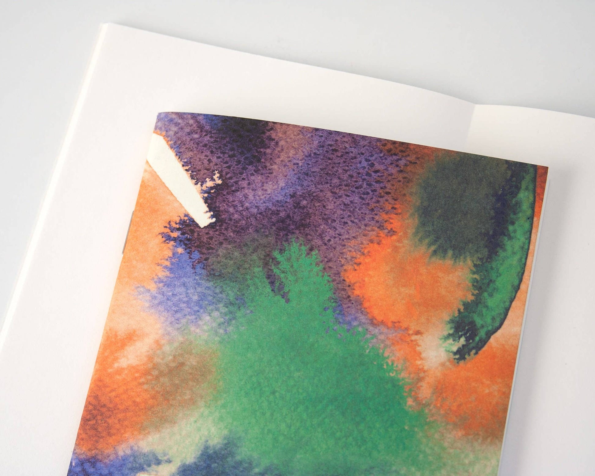 Das Papaya Paper Products | Notizheft A6 mit Aquarell/Watercolor-Motiv hat leere Seiten und einen FSC-zertifizierten abstrakten Einband in Grün, Orange, Lila und Blau. Es ruht auf einer weißen Oberfläche, ideal für nachhaltige Notizen.