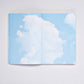 Ein aufgeschlagenes nuuna „Cloud Blue“-Inspirationsbuch in der Größe M von nuuna präsentiert 176 farbenfrohe Seiten, die mit einem blauen Himmel und flauschigen weißen Wolken bedruckt sind und so den Eindruck erwecken, man blicke in den Himmel – wodurch jeder Moment zu einem wahrhaft inspirierenden Erlebnis wird.