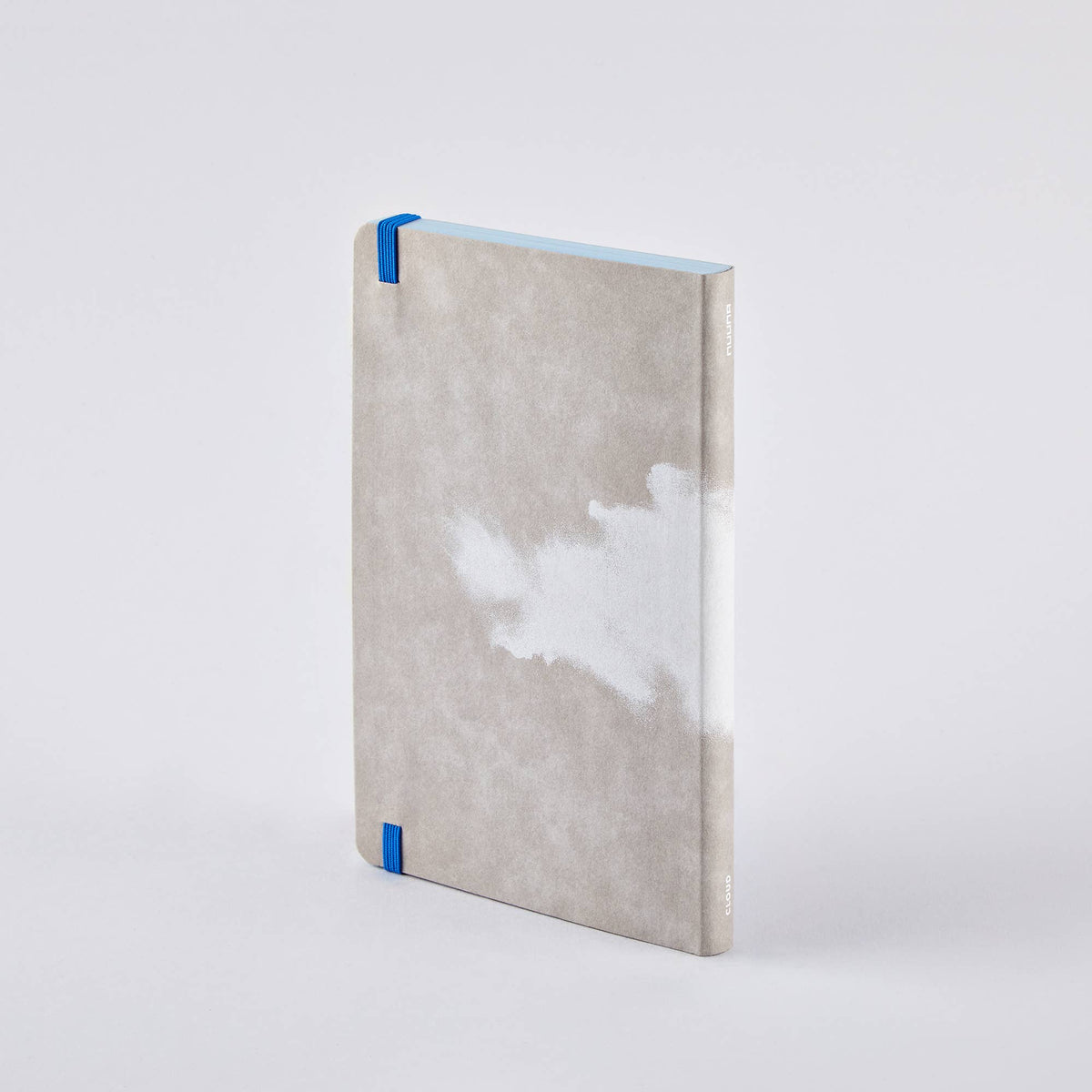 Ein geschlossenes nuuna | „Cloud Blue“-Inspirationsbuch in Größe M mit hellgrauem Einband und einem weißen, von Wolken inspirierten Muster, blauen Seitenrändern und blauen Eckschützern steht aufrecht vor einem schlichten weißen Hintergrund.