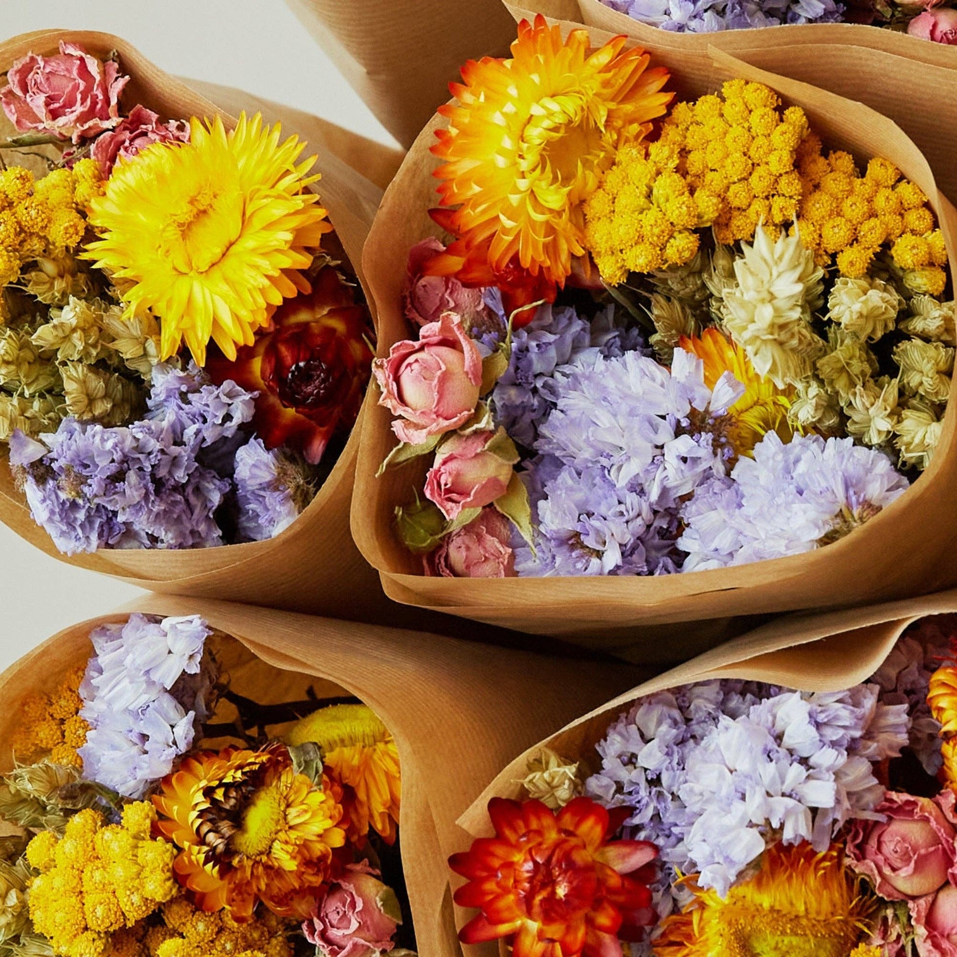 Fünf Sträuße mit Trockenblumen „Multicolor“ von Wildflowers by Floriette sind in braunes Papier eingewickelt und bestechen durch eine lebhafte Mischung aus gelben, orangefarbenen, lavendelfarbenen und rosa Blüten. Jeder Strauß aus der Wildflowers by Floriette-Kollektion verleiht jedem Raum einen fröhlichen Hauch von bunter Schönheit.
