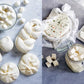 Eine Reihe von frischen Weißkäsesorten ist auf Marmor ausgestellt - links Mozzarellakugeln, -knoten und -rondellen und rechts Kräuterkäse in Gläsern - perfekt für die Herstellung von Rezepten oder hausgemachten Speisen mit der Speisekammer des Hölker Verlags.