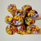 Zehn Sträuße aus Trockenblumen – mit gelben, violetten, orangefarbenen und rosa Blüten – sind in braunes Papier eingewickelt und auf einem schlichten, hellen Hintergrund kreisförmig angeordnet. Bei jedem Strauß handelt es sich um das Modell „Wildflowers by Floriette | Trockenblumen ‚Multicolor‘“ von Wildflowers by Floriette, das den für die Marke typischen natürlichen Charme wunderschön zur Geltung bringt.