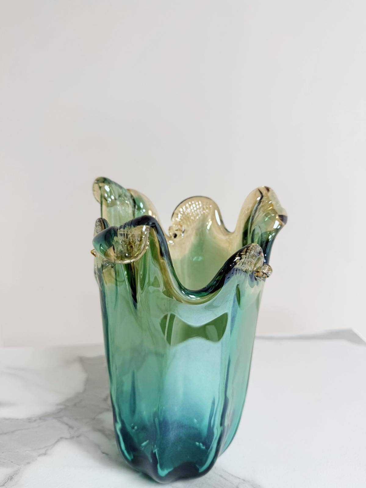 Die mittelgroße Vase „Venezia“ von Murano Dream aus grünem Murano-Glas (H 25 cm, Ø 14 cm) mit gewelltem Rand und gelben Akzenten besticht vor schlichtem Hintergrund durch ihre edle, künstlerische Ausstrahlung.