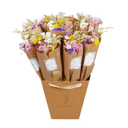 Eine braune Schachtel enthält sechs Sträuße „Wildflowers by Floriette“ | Trockenblumen „Dutch“ (ca. 50 cm), jeweils in braunes Papier mit dekorativen Etiketten eingewickelt. Diese langlebigen Trockenblumen von Wildflowers by Floriette zeichnen sich durch eine lebhafte Mischung aus rosa, weißen, gelben und violetten Blüten aus – perfekt für Ihren nächsten „Market More Bouquet“ oder ein einzigartiges Trockenblumenstrauß-Arrangement.
