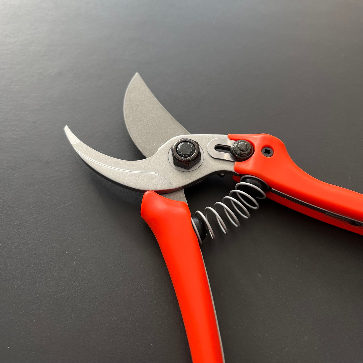 Die Löwe Original Löwe 14 - Economic Clean Cut Gartenschere verfügt über rote Griffe, eine Metallklinge und einen Federmechanismus – ideal für Gartenarbeit – dargestellt auf einer mattschwarzen Oberfläche.