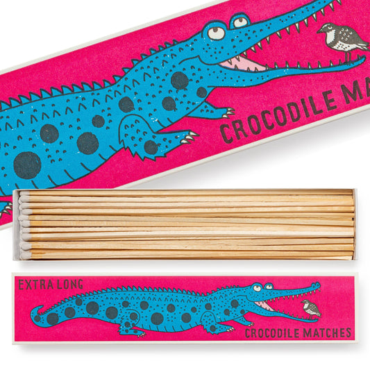 Die "Krokodil" Extra lange Streichhölzer von Archivist Gallery kommen in einer leuchtend rosa Schachtel mit einem blauen Cartoon-Krokodil und einem kleinen Vogel. Auf dem verspielten Design stehen die Worte "Krokodil Streichhölzer" und "Extra lang".