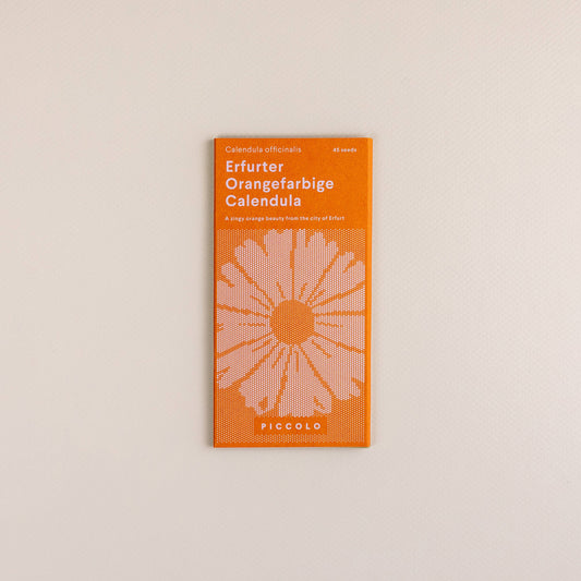Ein Päckchen Piccolo Seeds | Ringelblume Erfurter Orangefarbene von Piccolo Seeds, mit einem orange-weißen Design mit einer stilisierten Blumenillustration, ist auf einem hellbeigen Hintergrund platziert.