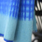 Eine Nahaufnahme der Blauen Tagesdecke "Darling" aus Lammwolle von Sofie Sjöström Design. Sie zeigt den gemütlichen, strukturierten Stoff mit einem blauen Verlaufsmuster, karierten Linien auf der Oberseite und einem einfarbigen hellblauen Rand auf der Unterseite.