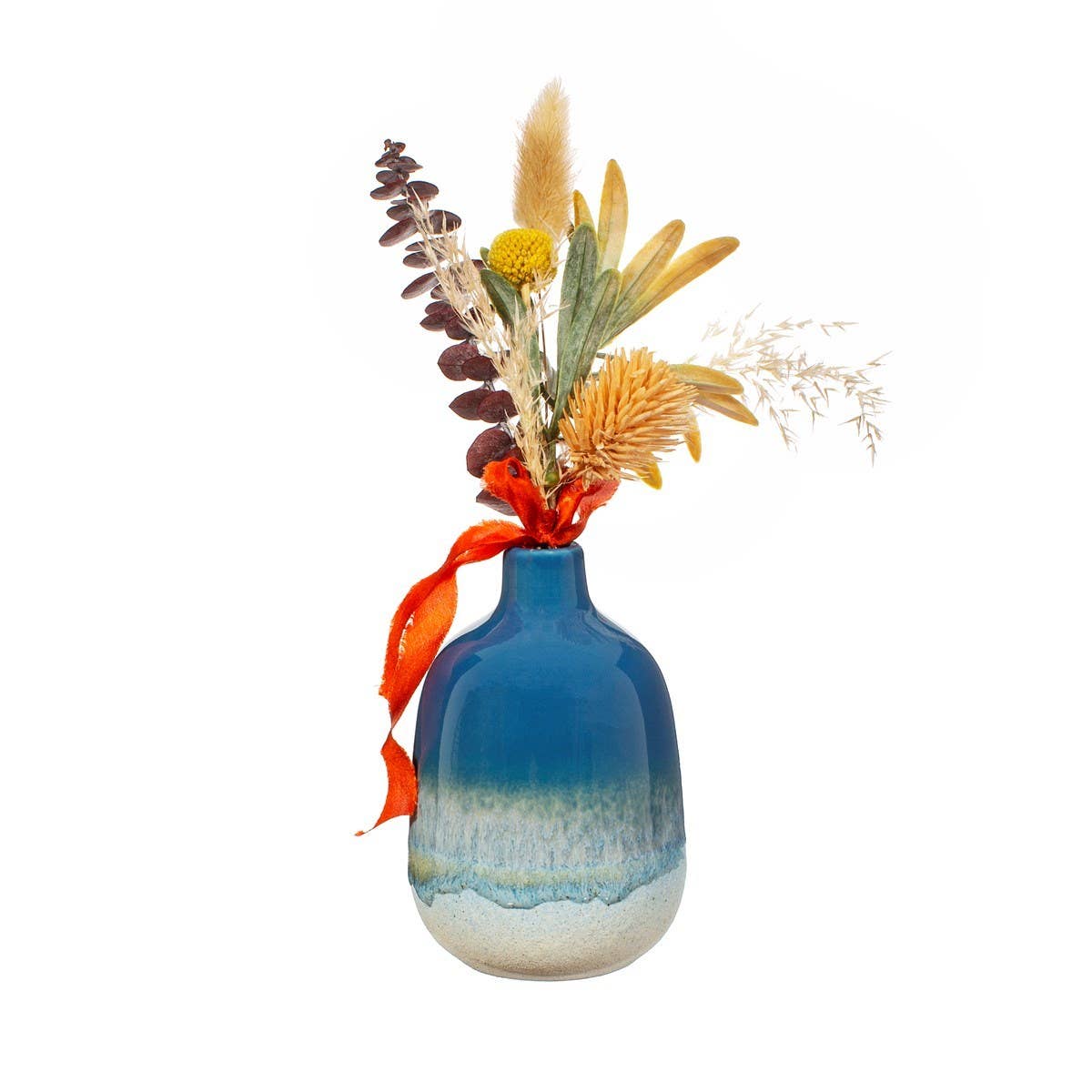 Sass & Belle Europe | Blaue Vase „Mojave Glaze“, 12,5 cm, präsentiert in einem sanften ozeanblauen Farbverlauf, gefüllt mit einer Auswahl getrockneter Blumen und Gräser in Gelb-, Braun- und Grüntönen. Mit einem orangefarbenen Band zusammengebunden, verleiht dieses Arrangement vor einem neutralen weißen Hintergrund einen Hauch von Boho-Charme.