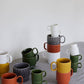 Zwei leuchtend gelbe Kaffeebecher der Sagaform GmbH aus dem 2-teiligen Set werden auf einer grauen Stoffoberfläche vor einer hellen Wand gestapelt und heben so ihre strukturierten Muster und ihr stilvolles skandinavisches Design hervor.