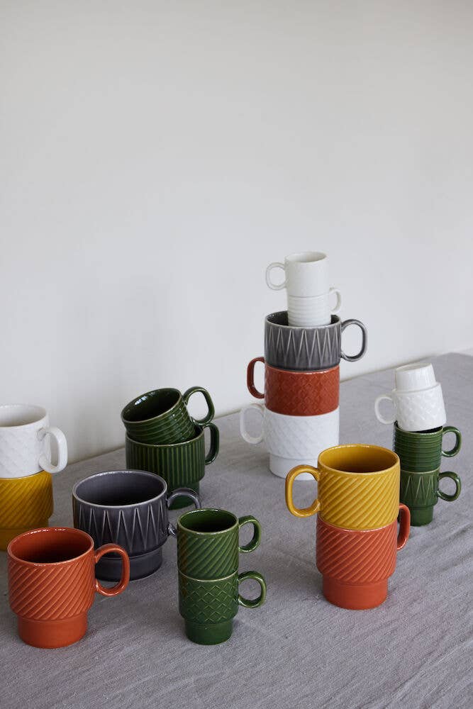 Zwei leuchtend gelbe Kaffeebecher der Sagaform GmbH aus dem 2-teiligen Set werden auf einer grauen Stoffoberfläche vor einer hellen Wand gestapelt und heben so ihre strukturierten Muster und ihr stilvolles skandinavisches Design hervor.