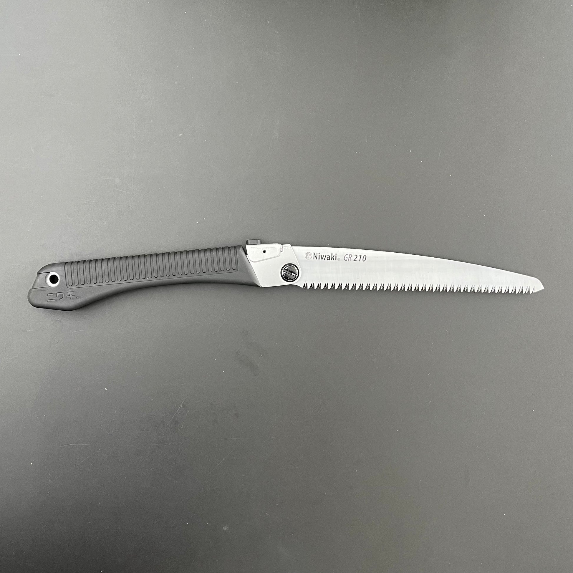 Die Niwaki | 'GR 210 Folding Saw' Klappsäge hat einen schwarzen Griff und eine silberne Klinge mit der Aufschrift "Niwaki GR-210", mit scharfen Zähnen - perfekt als Outdoorsäge oder für präzise Gartenschnitte. Teilweise geöffnet vor einem dunklen Hintergrund abgebildet.