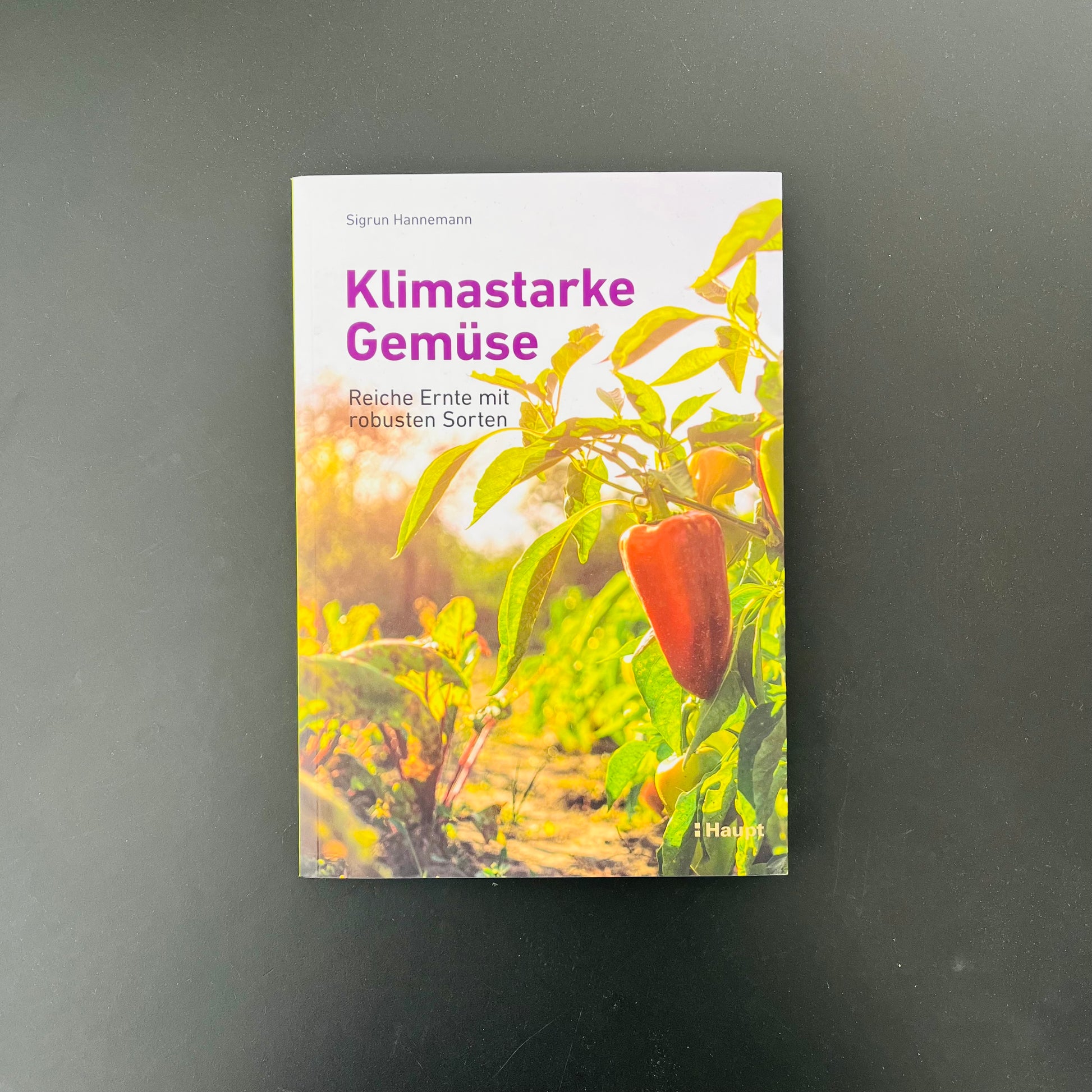 Das Buch - Klimastarke Gemüse aus dem Haupt Verlag ruht auf einer schwarzen Fläche, sein Cover zeigt sonnenbeschienene Gemüsepflanzen mit einer roten Paprika und dem Untertitel: Reiche Ernte mit robusten Sorten-ideal für den Gemüseanbau im Klimawandel.