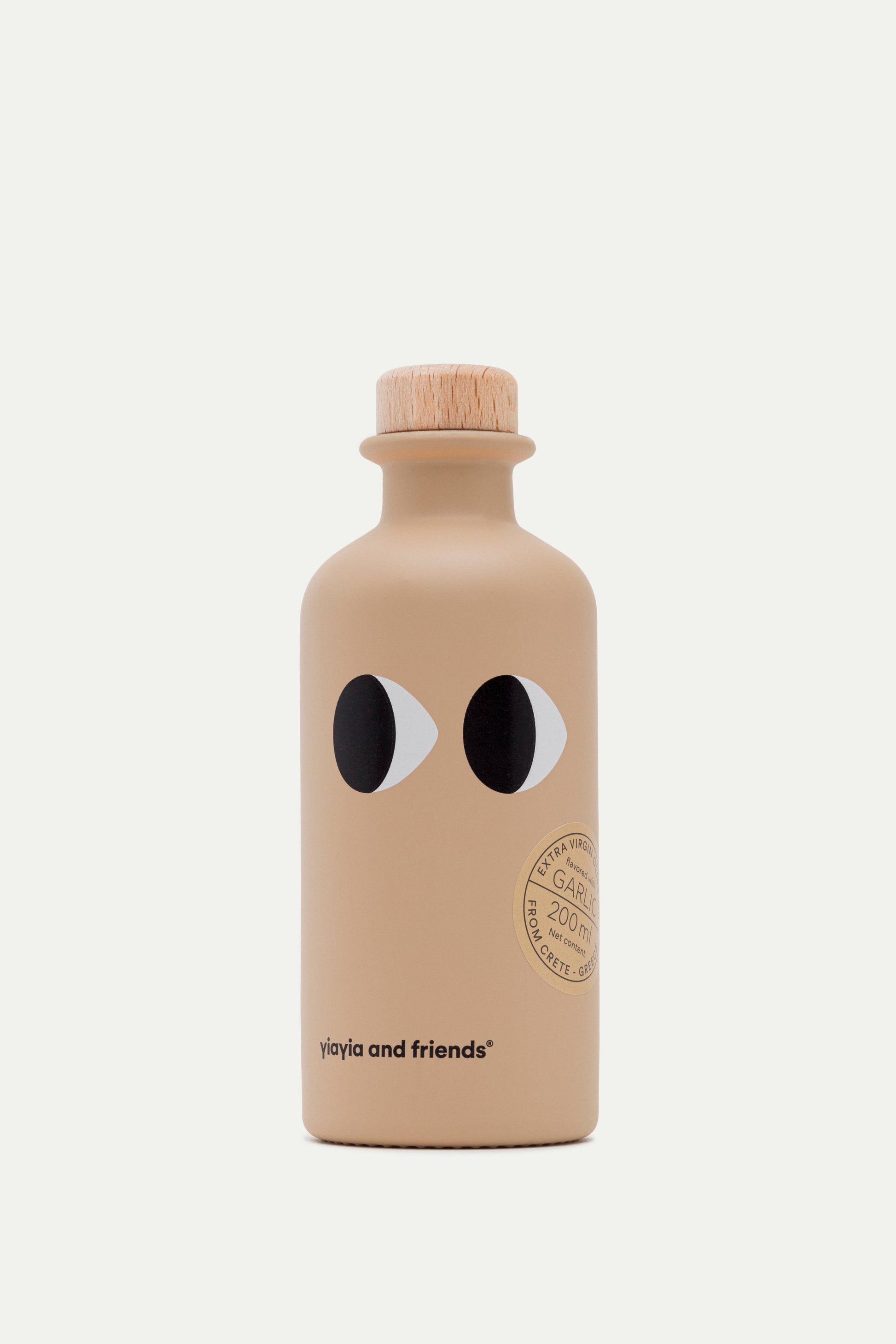 Eine beigefarbene Keramikflasche mit einem Holzdeckel, zwei Cartoon-Augen und dem Aufdruck "yiayia and friends" am Boden sowie einem runden Etikett für Yiayia and friends | Natives Olivenöl Extra mit Knoblauch 200 ml. Abgebildet auf einfarbig weißem Hintergrund.