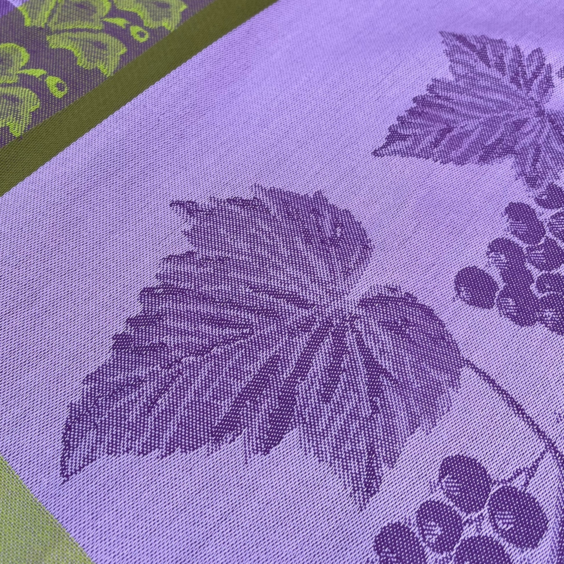 Nahaufnahme des Garnier Thiebaut Geschirrtuchs 'Les Cassis Mauve', mit einem gewebten Traubenblatt- und Traubenmuster aus mauvefarbener Baumwolle, akzentuiert mit einer grünen Bordüre und einem passenden Traubenmotiv.