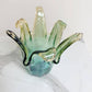 Die Murano Dream „Giusy“-Vase aus grünem Murano-Glas (H 24, Ø 18 cm) besticht durch handgefertigte, wellenförmige Kanten und setzt auf weißem Marmor vor hellem Hintergrund elegante Akzente in jedem Raum.