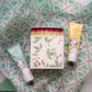 Zwei Tuben Archivist | 'Sheabutter' Handcreme von Archivist Gallery neben einer dekorativen Streichholzschachtel mit Erdbeerdesign - arrangiert auf gemustertem Papier mit grünen Blättern und roten Erdbeeren.