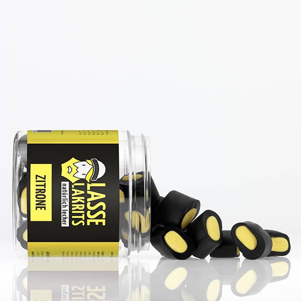 Eine Dose LASSE LAKRITS | Dose Lakritz Zitrone liegt auf der Seite und verschüttet schwarze und gelbe Bonbons. Auf dem Etikett stehen die Marke LASSE LAKRITS, der Satz "natürlich lecker" und eine Zeichentrickfigur.