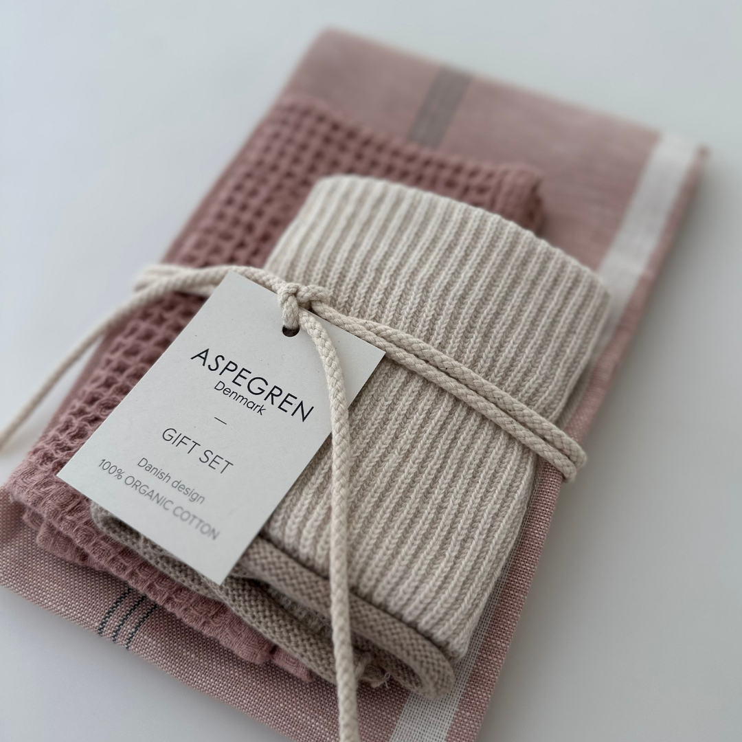 Ein Set aus drei Küchentüchern von Aspegren Denmark in warmen Rosatönen, ordentlich gefaltet und mit einer cremefarbenen Kordel zusammengebunden. Auf dem Etikett steht: „ASPEGREN Denmark GIFT SET Danish design 100 % ORGANIC COTTON.“.