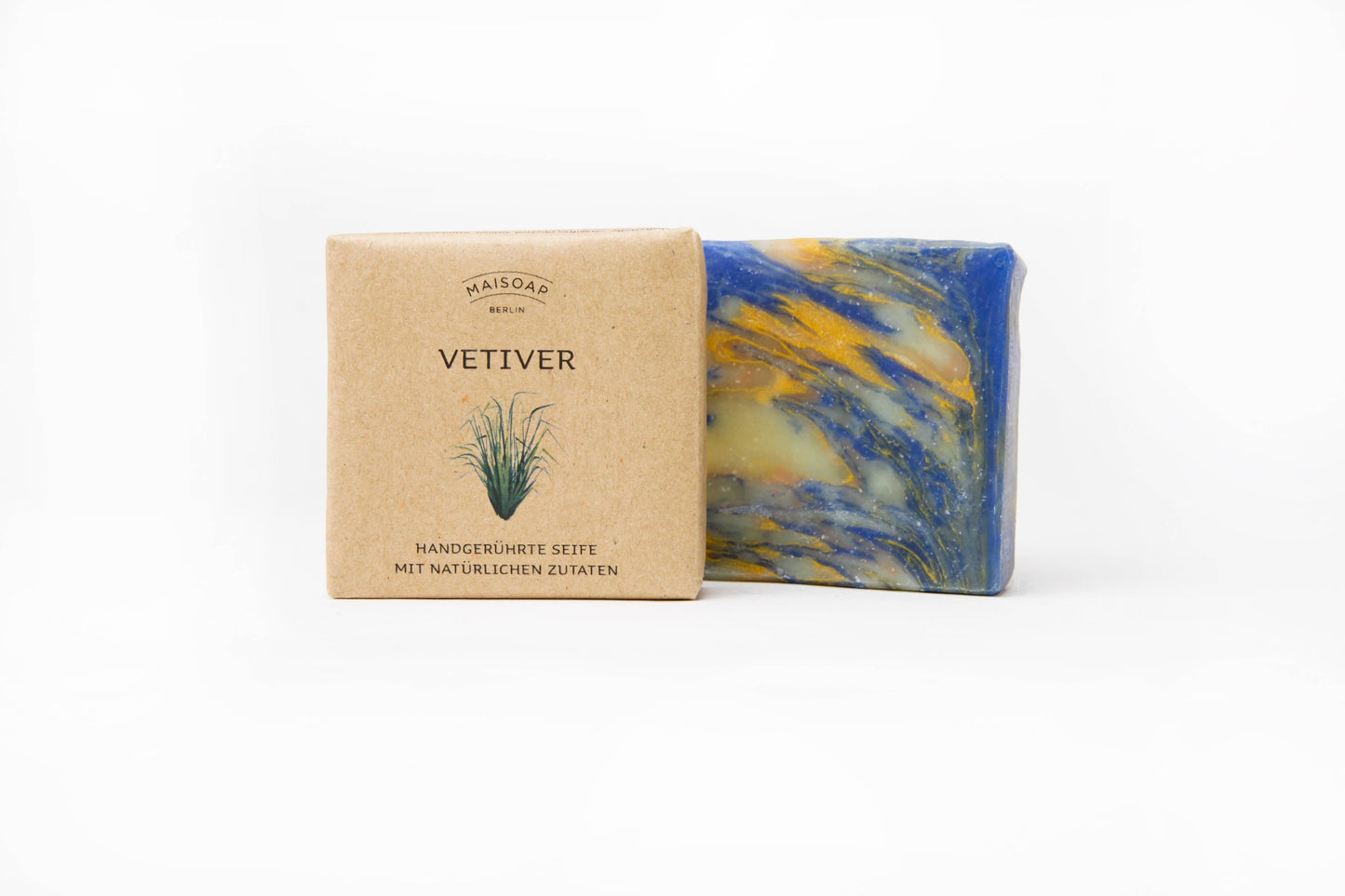 Ein Stück Maisoap | Vetiver Seife mit blauen, gelben und weißen Strudeln ruht neben seiner braunen Papierverpackung mit der Aufschrift "Maisoap | Vetiver Seife" - eine handgemachte Seife mit natürlichen Inhaltsstoffen, einem Hauch von Bergamotte und einer kleinen Pflanzenillustration.