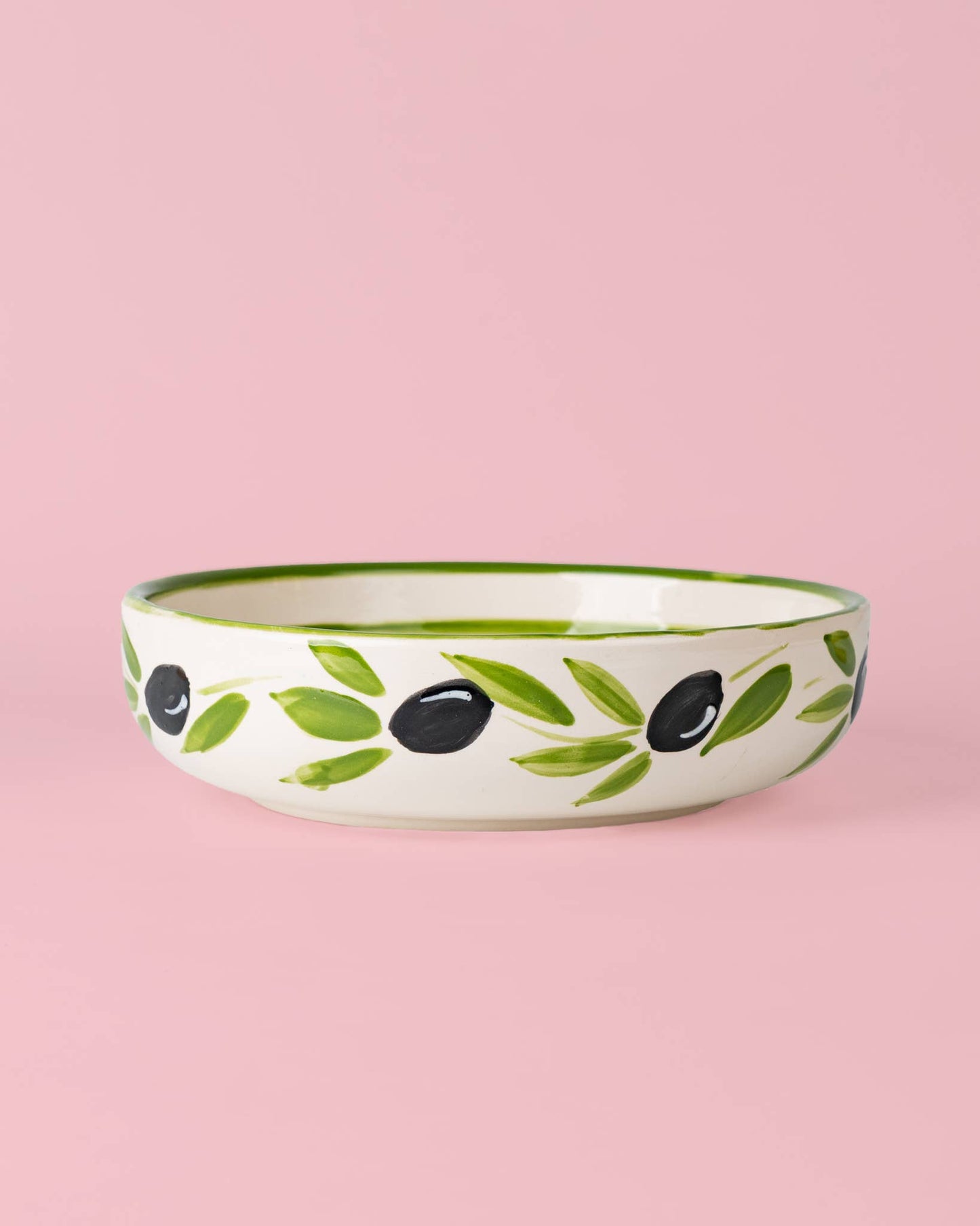 Eine Keramikschale von Alfar Tierra Cocida, die „Große Keramik Reibplatte Olive“, von Hand mit grünen Blättern und schwarzen Oliven bemalt, steht auf einem hellrosa Hintergrund und versprüht mediterranen Charme.