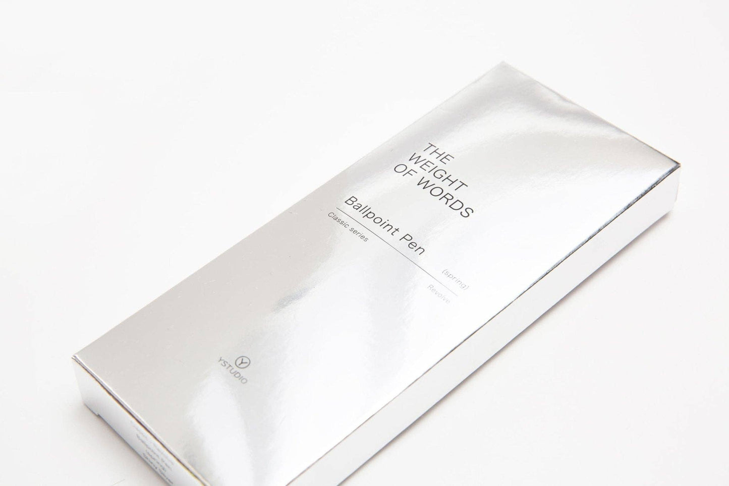 Eine silbern glänzende Schachtel mit der Aufschrift YSTUDIO | Klassischer Drehkugelschreiber Feder (Glänzendes Silber) von ENTREPÔT, in minimalistischem Design, steht als exklusive limitierte Auflage auf einem makellosen weißen Hintergrund.