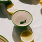 Eine kleine Keramikschale „Olive“ von Alfar Tierra Cocida | Handgefertigte kleine Keramikschale von Alfar Tierra Cocida mit grünem Rand und Blattmotiv steht auf einer Tischdecke neben Zitronenscheiben. Handgefertigt in Spanien, fängt die mediterrane Keramikschale das Sonnenlicht ein und wirft sanfte Schatten auf die Szenerie.
