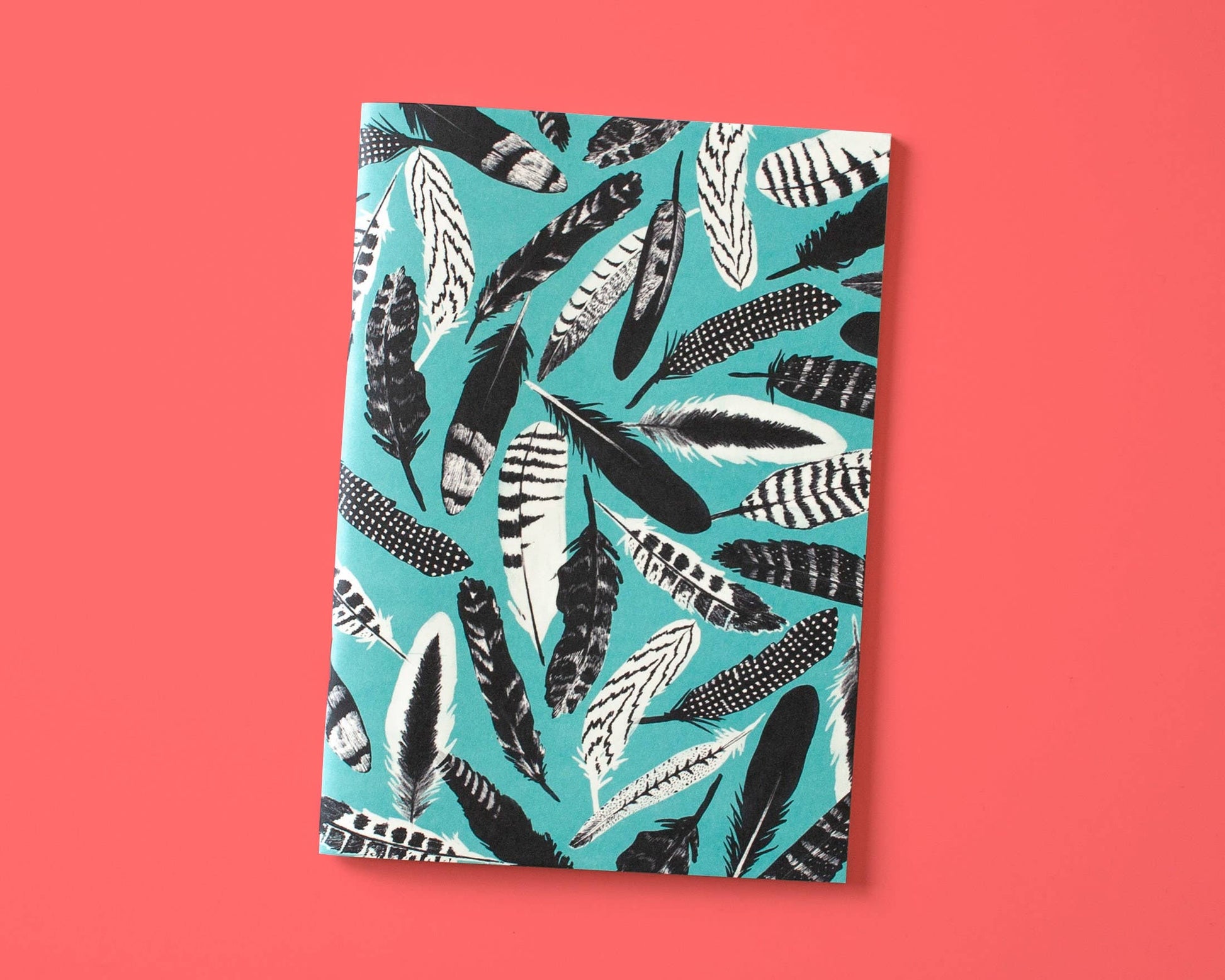 Das Papaya Paper Products | Notizheft A5 mit Federmuster blau von Papaya Paper Products zeichnet sich durch ein blaues Federmuster auf dem Einband aus, das auf einem korallenrosa Hintergrund ruht, und verwendet Munken Print Cream Papier für eine stilvolle, nachhaltige Note.