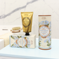 Eine goldene Handcremetube und eine Schachtel Panier Des Sens Pflanzliche Seife Meerfenchel 150 g stehen auf einer hellblauen Fläche mit einer Marmorwand und einer Bürste im Hintergrund.