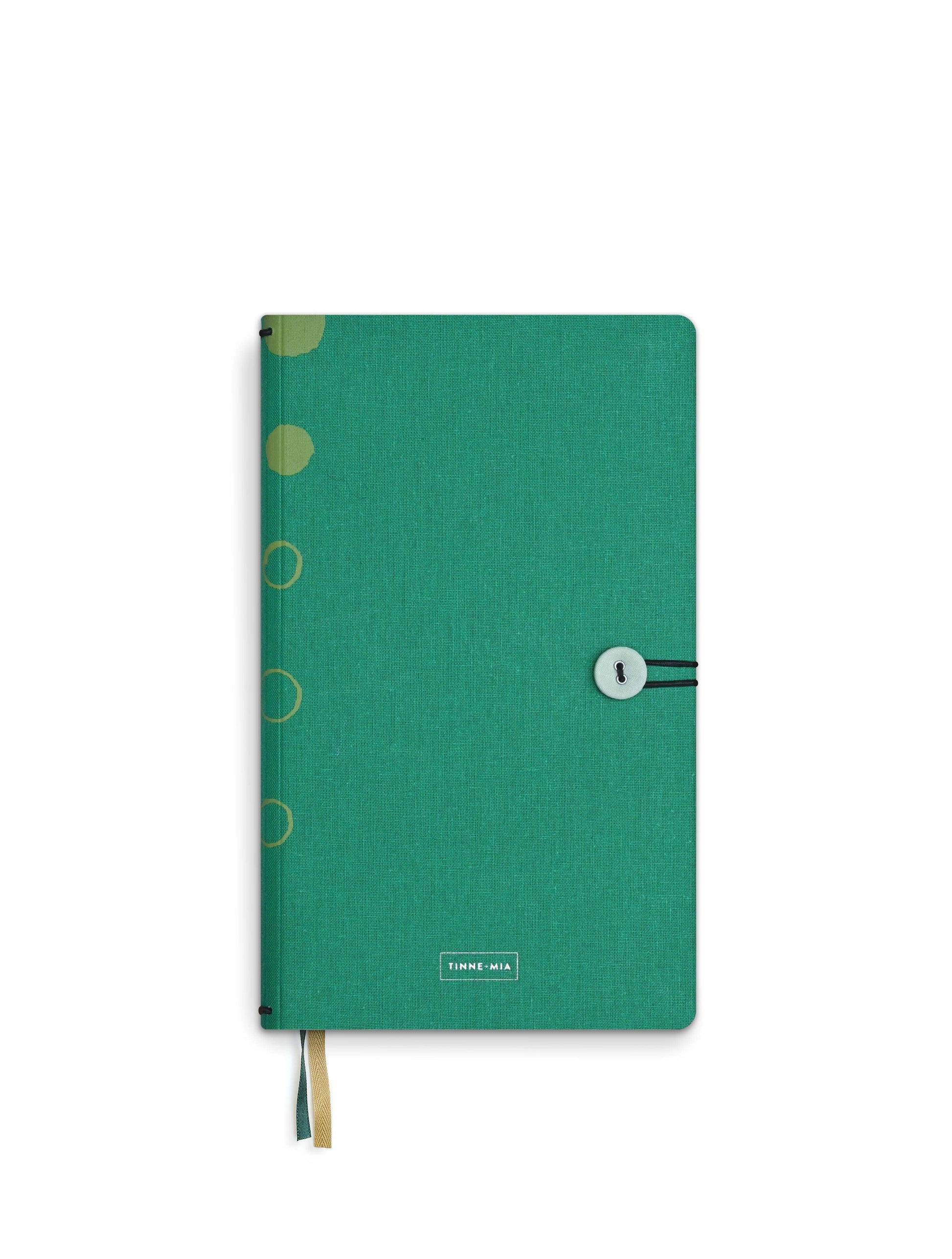 Das Tinne Mia Notizbuch mit Knopf 'Leinen Smaragd' von Tinne Mia ist ein grünes FSC-zertifiziertes Hardcover-Notizbuch mit kreisförmigen Motiven am linken Rand, Gummiband und Knopfverschluss, zwei Lesebändchen - ideal als Tagebuch oder Bullet Journal. Abgebildet auf weißem Hintergrund.