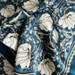 Eine Nahaufnahme des von William Morris inspirierten Koustrupco | Seidenschal Morris Pimpernel Blau 50 x 50 cm zeigt große cremefarbene Blumen, dunkelgrüne Blätter und goldene Details auf einem dunkelblauen Hintergrund; der Seidenschal wirkt weich und leicht gefaltet.