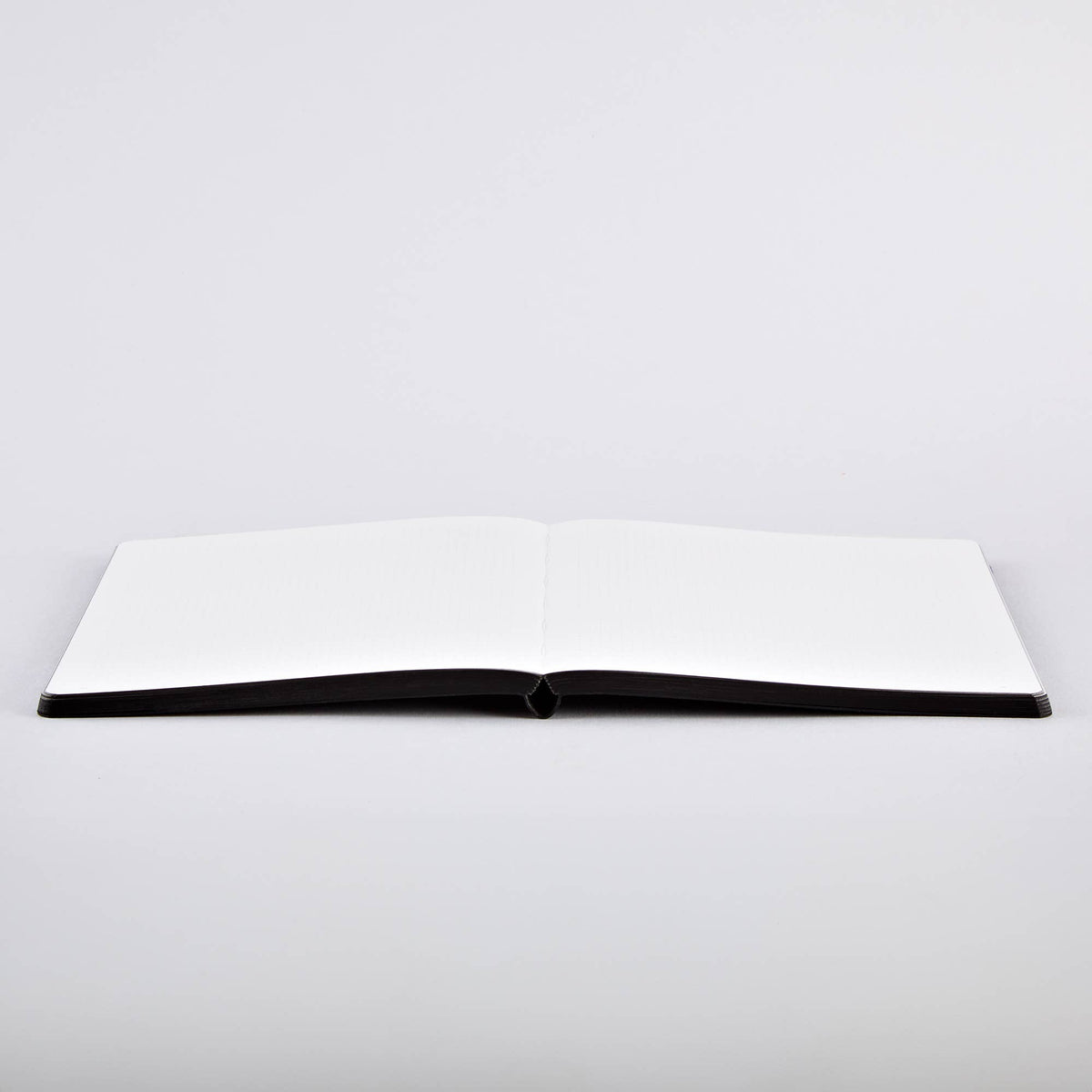 Ein aufgeschlagenes Nuuna-Notizbuch „Sassy Squares“ Notizbuch Not Ordinary L Light A5+ liegt mit nach oben gerichteten, völlig leeren Seiten auf einer weißen Fläche.