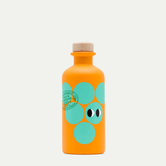Eine leuchtend orangefarbene 200-ml-Flasche von yiayia and friends mit einem Holzdeckel, türkisfarbenen Kreisen und augenähnlichen Motiven, beschriftet mit "Weißer Balsamico-Essig" - ideal für Vinaigretten oder Salate.