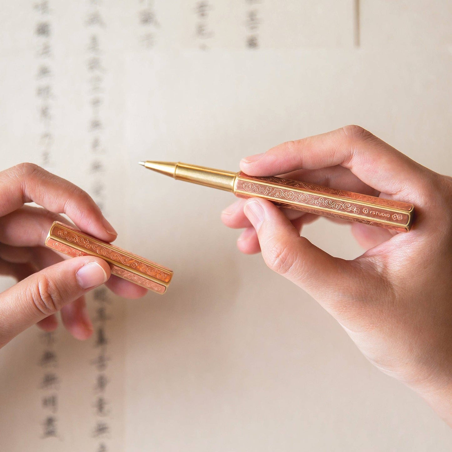 Zwei Hände halten den ENTREPÔT YSTUDIO | Klassische Renaissance KAZARI KANAGU ORCHID Tintenroller und dessen Kappe über Papier mit chinesischer Kalligraphie, was auf eine laufende Schrift oder Kalligraphie hindeutet.