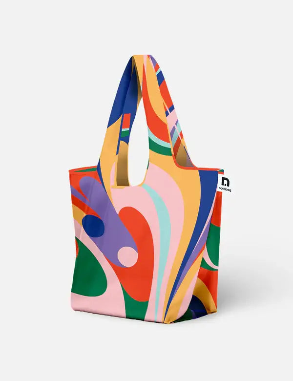 Die Notabag | Shopping Tote 'Flow' von Notabag zeigt ein farbenfrohes abstraktes Wirbelmotiv in Gelb, Rosa, Rot, Grün, Blau und Lila auf einer wiederverwendbaren Tasche. Fotografiert auf Weiß. Die faltbare Einkaufstasche vereint Stil und Funktion.