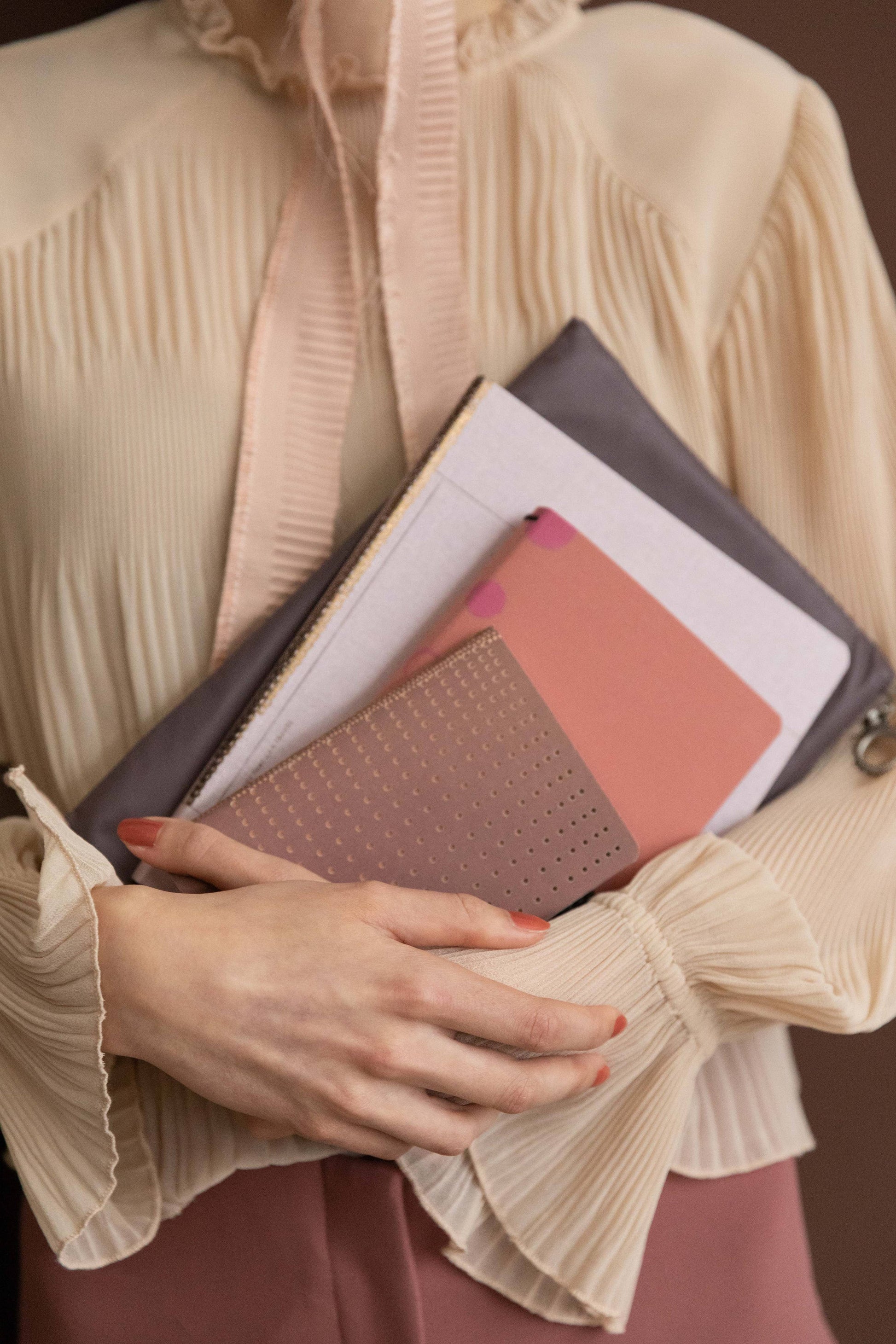 Eine Person in cremefarbener Bluse hält mehrere pinke und mauvefarbene Notizbücher sowie das Tinne Mia Bullet Journal A6 'Grid Burgunderrot' aus FSC-zertifiziertem Papier, die Hände sanft auf das gepunktete Raster gelegt.