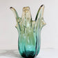 Die mittelgroße Vase „Giusy“ von Murano Dream (H 24, Ø 18 cm) aus grünem Murano-Glas besticht durch ihre abstrakte, organische Form und ihre edle Farbgebung – ein elegantes Designstück für stilvolle Räume.