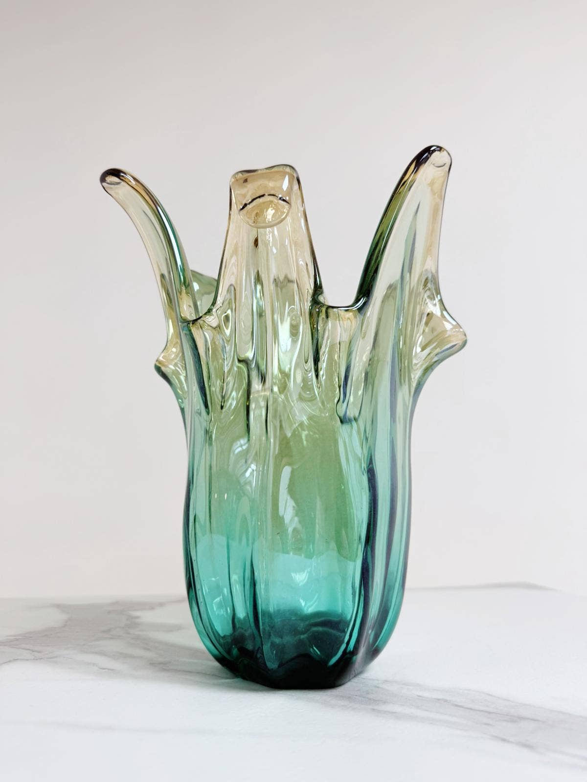 Die mittelgroße Vase „Giusy“ von Murano Dream (H 24, Ø 18 cm) aus grünem Murano-Glas besticht durch ihre abstrakte, organische Form und ihre edle Farbgebung – ein elegantes Designstück für stilvolle Räume.