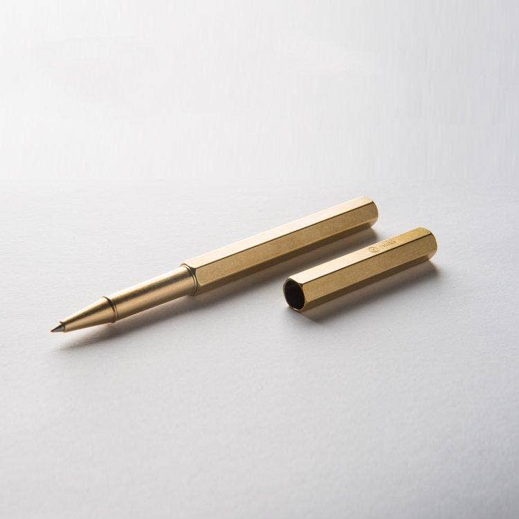 Ein goldener, sechseckiger YSTUDIO Klassischer Revolve-Rollerball-Stift (Messing) von ENTREPÔT, Kappe entfernt und daneben auf einer weißen Fläche platziert - entworfen für sanftes Schreiben und stabilen Griff.