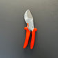 Eine Gartenschere vom Typ Löwe Original Löwe 10 – mit leuchtend orangefarbenen Griffen und einer silbernen Klinge auf dunklem, einfarbigem Hintergrund.