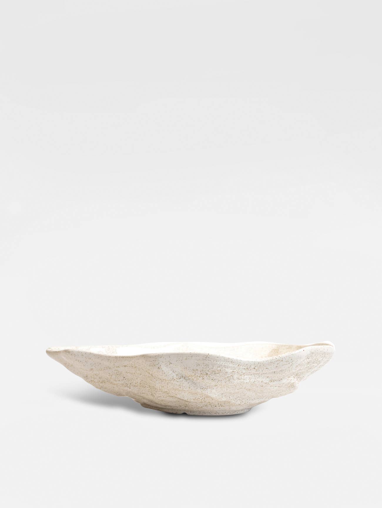 Die BYON Design Schale Alima von Sagaform GmbH ist eine flache, ovale Bone China Schale in Beige mit einer organischen, ungleichmäßigen Form und einer gesprenkelten, cremefarbenen Oberfläche, die vor einem schlichten, hellen Hintergrund gezeigt wird.
