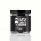 Eine durchsichtige Plastikdose LASSE LAKRITS Dose Lakritz Süß natürlich lecker mit einem schwarzen Deckel enthält schwarze Lakritze. Auf dem Etikett steht "LASSE LAKRITS natürlich lecker" und "Lakritz Süß", mit einem bärtigen Mann Logo auf schwarzem Hintergrund.